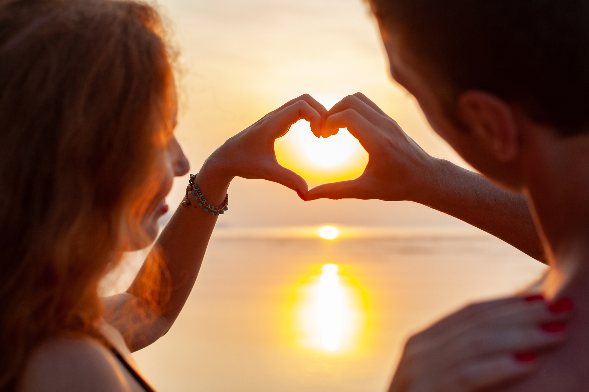 Couple forming heart shape at sunset.
